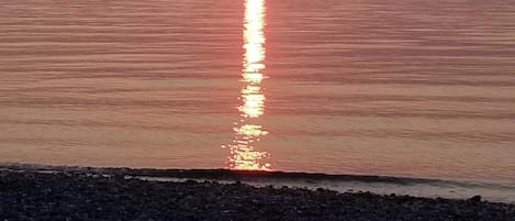 A sunset over a calm sea with a rocky shoreline.