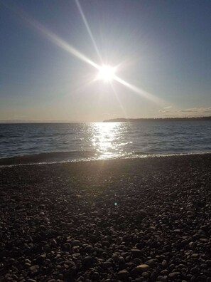 Een strand met kiezels en de zon die over het water schijnt.