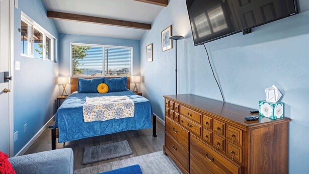 A bedroom with a bed, wooden dresser, and a TV mounted on the wall. - Studio with covered deck and Birch Bay View (Blaine)