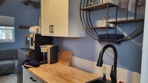 A compact kitchen with a wooden countertop, a sink, and a microwave. There is a window with blinds, a sofa, and a circular shelf with glasses and a candle. - Studio with covered deck and Birch Bay View (Blaine)