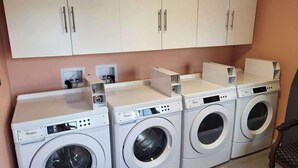 A laundry room with four front-loading washers and dryers, a wooden chair, and a white cabinet above the machines.