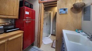 A compact kitchen with a red refrigerator, a shower, and a white bathtub.