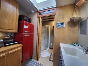 Cocina compacta con refrigerador rojo, ducha y bañera blanca.