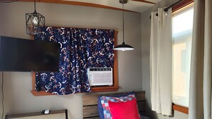 Ein Schlafzimmer mit Bett, Schreibtisch, Stuhl, einem Fenster mit Vorhängen und einer Pendelleuchte.