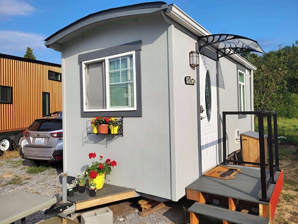 A small, single-story mobile home with a white exterior, a window, a door, and a small porch area.