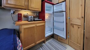 A compact kitchen with wooden cabinets, a red microwave, and a built-in refrigerator.