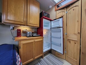 Cocina compacta con armarios de madera, un microondas rojo y un refrigerador empotrado.