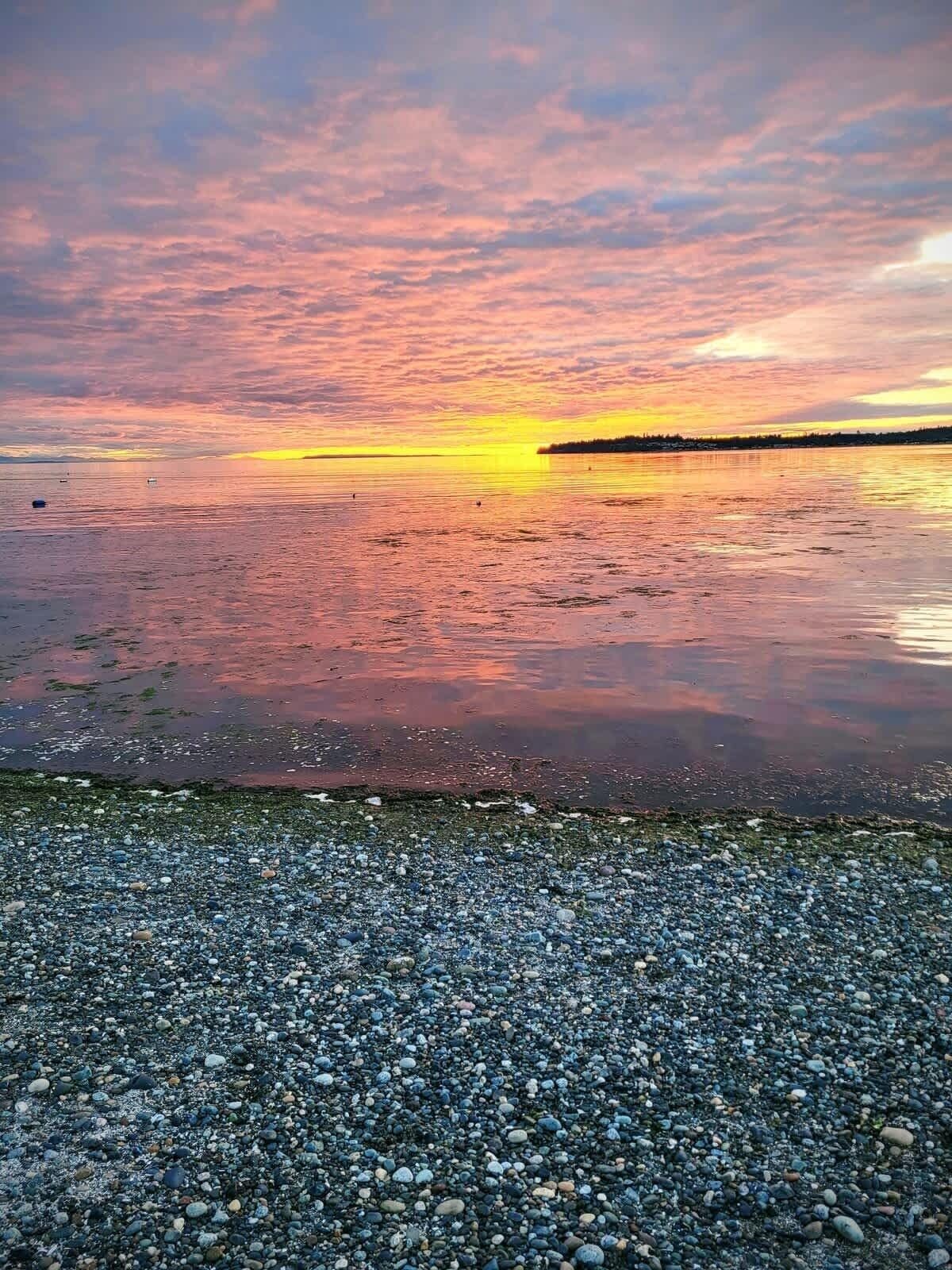 A pebbled beach with a sunset over a calm body of water.