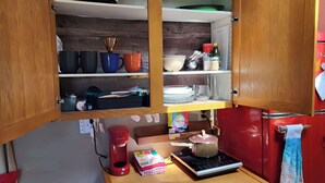 Eine kleine Küche mit Holzschränken, einer Kaffeemaschine, einem Wasserkocher und einem Tisch mit einer bunten Tischmatte.