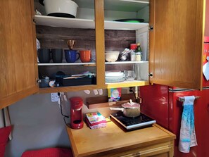 A compact kitchen with wooden cabinets, a coffee maker, a kettle, and a small table with a colorful mat.