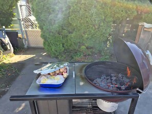 Ein Grill mit einem in Alufolie gewickelten Tablett voller Speisen und einer Grillpfanne mit sichtbaren Flammen.