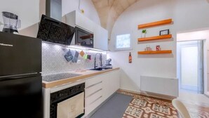 A compact kitchen with a black refrigerator, a microwave, and a sink. There are wooden shelves on the wall and a patterned rug on the floor. - Historic Holiday Home Il Melograno where tranquility reigns supreme (cavallino)
