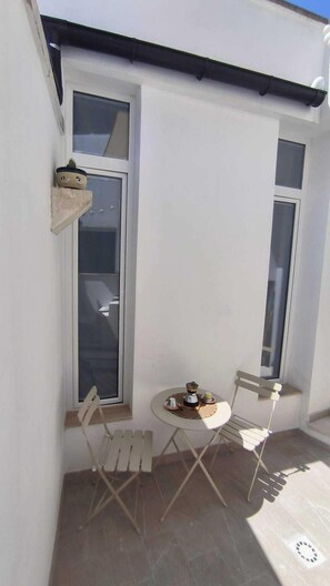 Un petit espace extérieur aménagé avec une table et deux chaises, un pot de fleurs et une fenêtre.