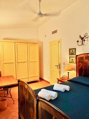A bedroom with a bed, a chair, a wardrobe, and a nightstand with a lamp.
