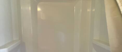 A white shower enclosure with a showerhead, a small shelf, and two clear glass shower knobs.