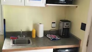 Et lille køkken med hvide skabe, en mikrobølgeovn, kaffemaskine og vask.