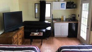 En kompakt opholdsstue med fjernsyn, sofa og tekøkken.