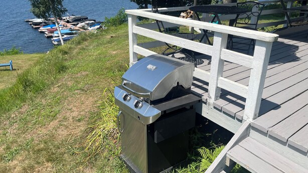 En træterrasse med grill, udsigt over en sø med fortøjede både.