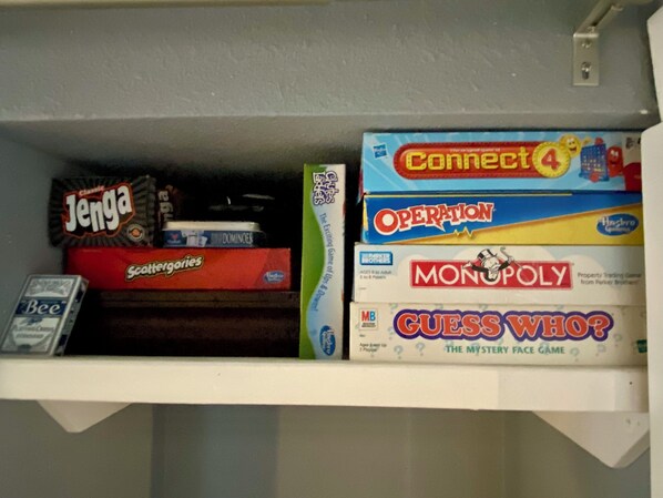 Una estantería con varios juegos de mesa, incluyendo Connect 4, Monopoly y otros.