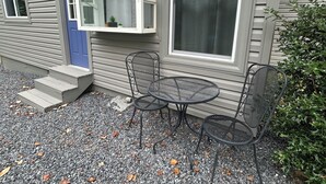 A house with a blue door, a window with a white frame, and a small patio with a table and two chairs. - Welcoming 3-bedroom house near charming Mount Ida and Lake Ouachita! (Mount Ida)