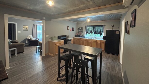 A spacious living area with a kitchen, wooden flooring, and a dining table with bar stools. - Welcoming 3-bedroom house near charming Mount Ida and Lake Ouachita! (Mount Ida)