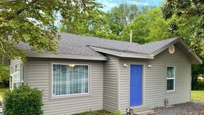 A small, single-story house with a blue door, a window with a curtain, and a small porch area. - Welcoming 3-bedroom house near charming Mount Ida and Lake Ouachita! (Mount Ida)