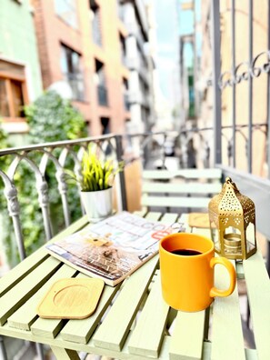 Ein Balkon mit Holztisch, gelber Tasse, Zeitschrift, kleiner Pflanze und dekorativer Laterne.