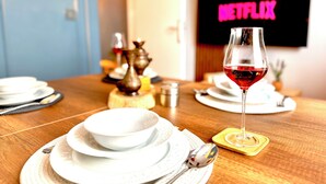 Una mesa de comedor con platos, una copa de vino tinto y un cartel de Netflix al fondo.