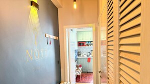 Un pasillo con un banco, una pared con una placa con nombre, y una cocina visible a través de una puerta abierta.