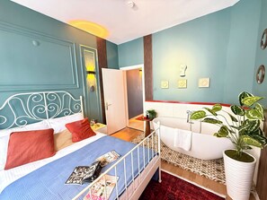 Ein Schlafzimmer mit einem Bett, einem Nachttisch, einem roten Teppich, einer weißen Badewanne und einer Topfpflanze.