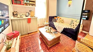 Un espacio habitable compacto con kitchenette, un sofá, una mesa de centro y un televisor de pantalla plana.