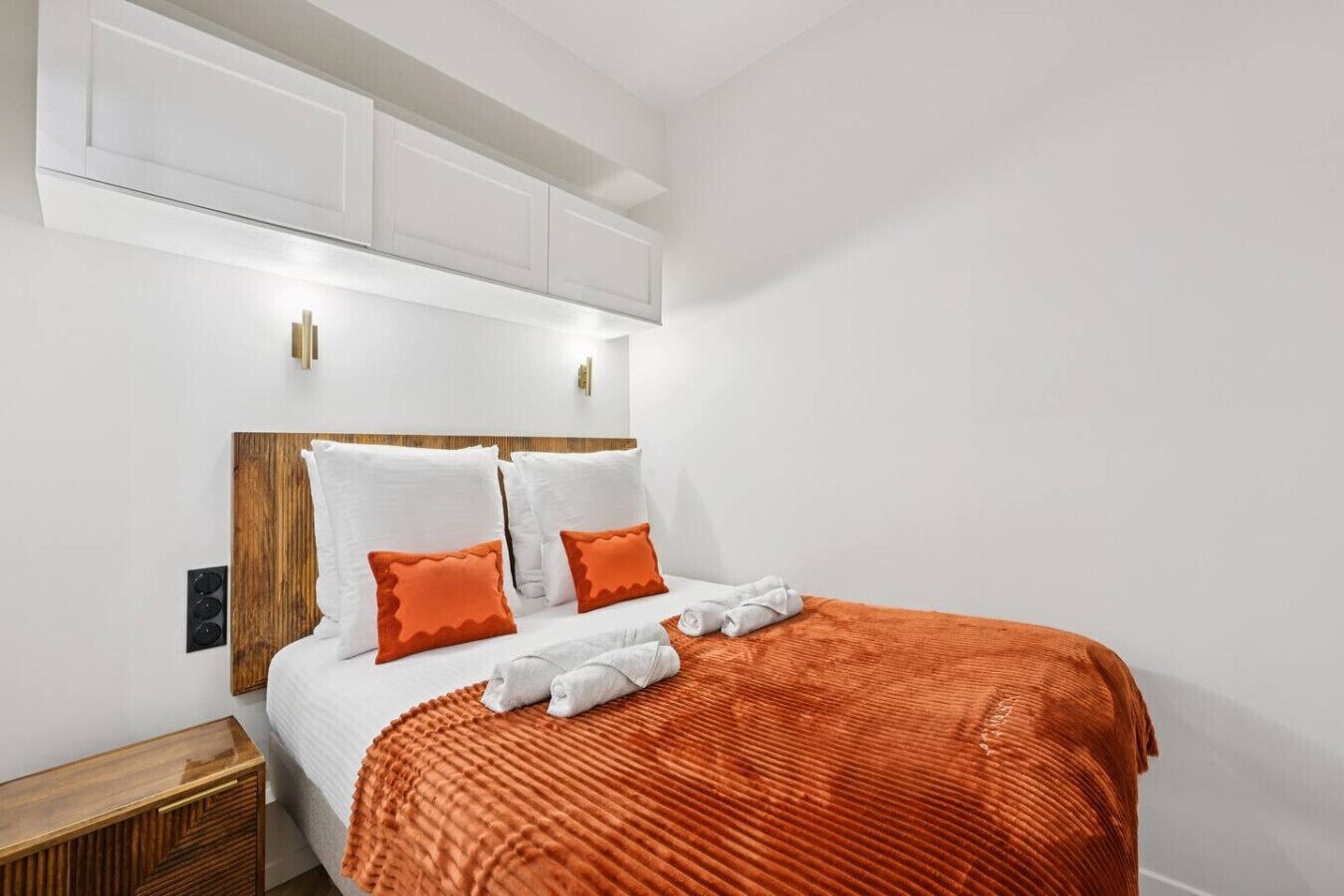 A bedroom with a wooden headboard, white bedding, and orange pillows.