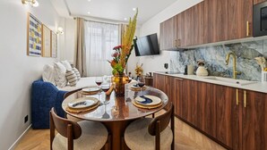 A modern kitchen with wooden cabinets, a marble countertop, and a dining area with a round table set for two. - Lavie Maison : Hot Tub & AC (Paris)