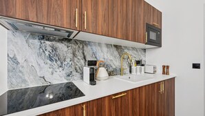 A kitchen with wooden cabinets, a white countertop, a marble backsplash, a built-in microwave, and a kettle. - Lavie Maison : Hot Tub & AC (Paris)