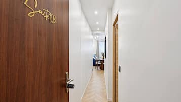 Un couloir mène à une porte en bois portant l’inscription « Suite 103 », qui donne sur une pièce contenant un bureau et une chaise.