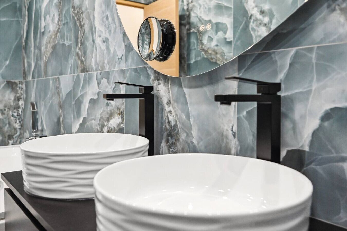 Un baño moderno con dos lavamanos de cerámica blanca y grifos negros, sobre un elegante salpicadero de mármol.