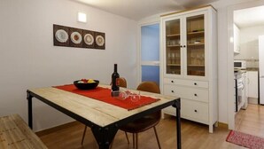 Un comedor con una mesa de madera, un posavaso rojo y un cuenco de fruta. Se aprecia un armario con puertas de vidrio al fondo.