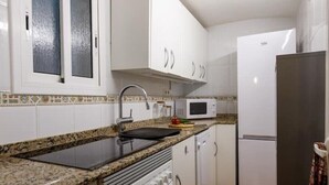 Una cocina compacta con armarios blancos, un microondas, una estufa y un refrigerador.