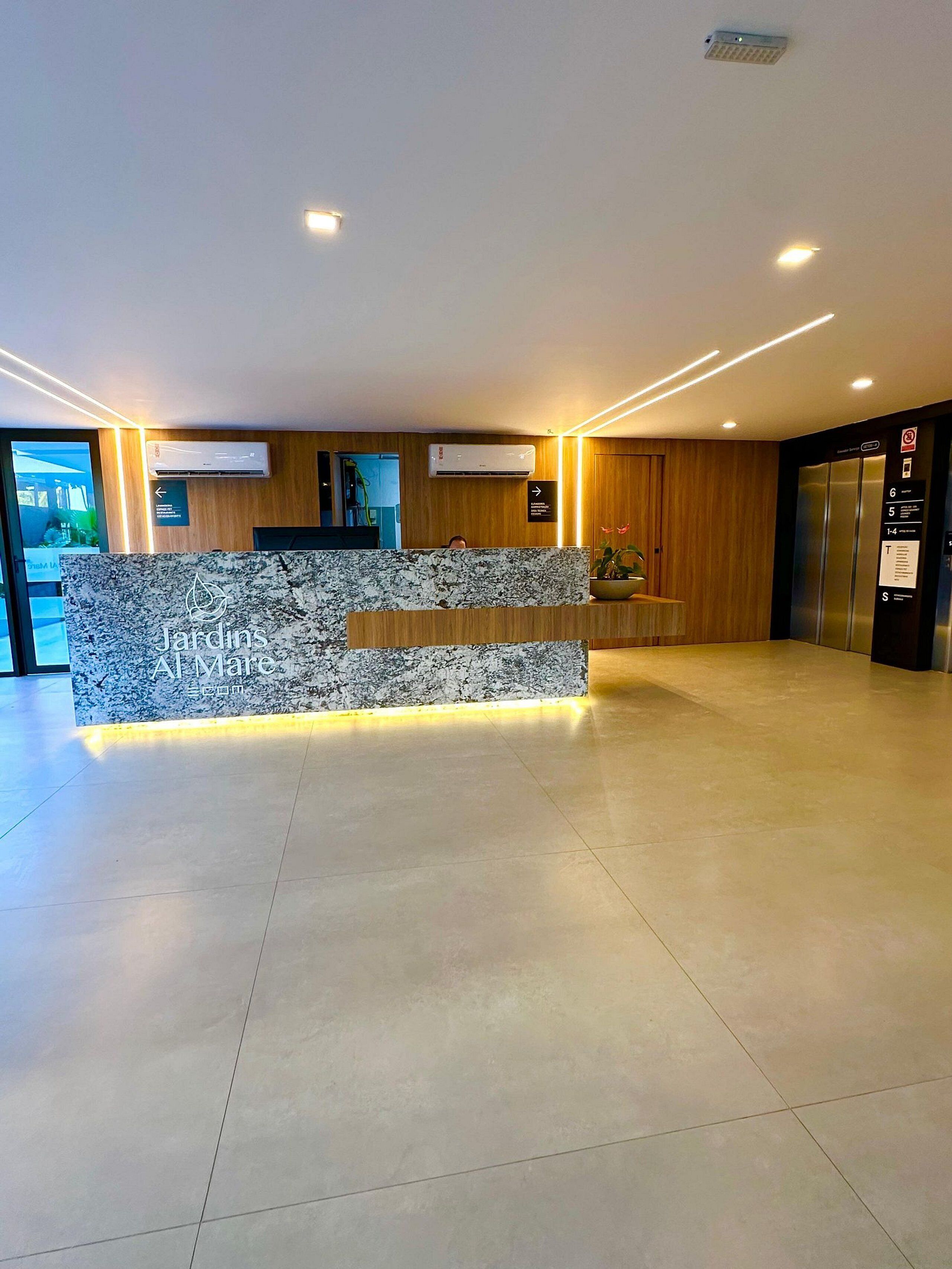 Una reception con piano in marmo, condizionatori, una parete in legno e un display digitale.