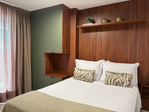 Une chambre à coucher avec un lit, des oreillers, une étagère avec des objets décoratifs et un mur vert.