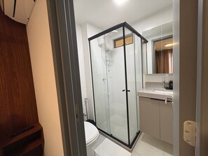 Moderni kylpyhuone, jossa on lasiseinällä varustettu suihku, wc ja peilillä varustettu pesuallas.
