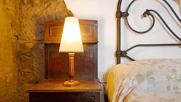 A wooden bedside table with a lamp, a metal headboard, and a floral bedspread.