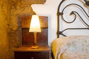 A wooden bedside table with a lamp, a metal headboard, and a floral bedspread. - Authentic Canarian House in the Center of Gran Canaria (Tejeda)