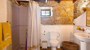 A bathroom with a stone wall, a shower, a toilet, and a sink.