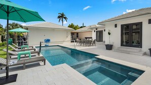 Una piscina con sillones de playa y una mesa, rodeada de un patio con una zona de estar cubierta.