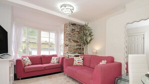 A living room with two pink sofas, a stone fireplace, a television, and a glass table. - Stargazy (Tintagel)