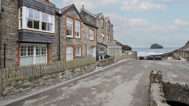 A coastal street lined with stone buildings, featuring a clear view of the sea and a distant island. - Stargazy (Tintagel)