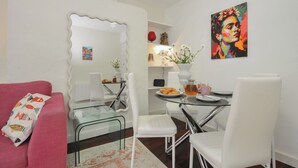 A modern living room with a glass coffee table, white chairs, a pink sofa, and a dining area with a white table and chairs. - Stargazy (Tintagel)
