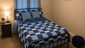 A bedroom with a checkered bedspread, a nightstand with a lamp, a ceiling fan, and a wall-mounted picture. - Pet-Friendly 4 bed Home w/ Pool Access, Patio & Garage – Walk to Dining! (Gilbert)