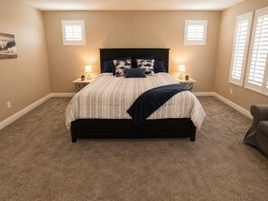 Une chambre à coucher avec un lit, deux tables de chevet, une chaise et une fenêtre avec des stores.